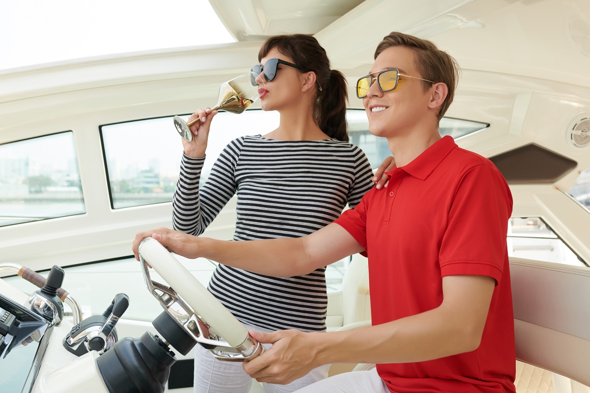 Positive wealthy young couple riding on sail boat or yacht floating in sea