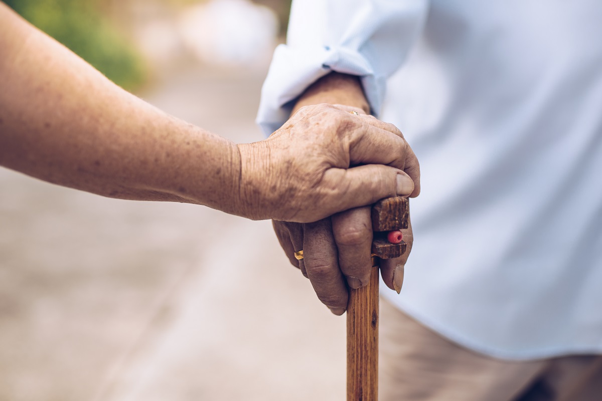 Close up of elderly hands in wrinkles holding walking stick.elderly old man with walking stick stand on footpath sidewalk crossing.