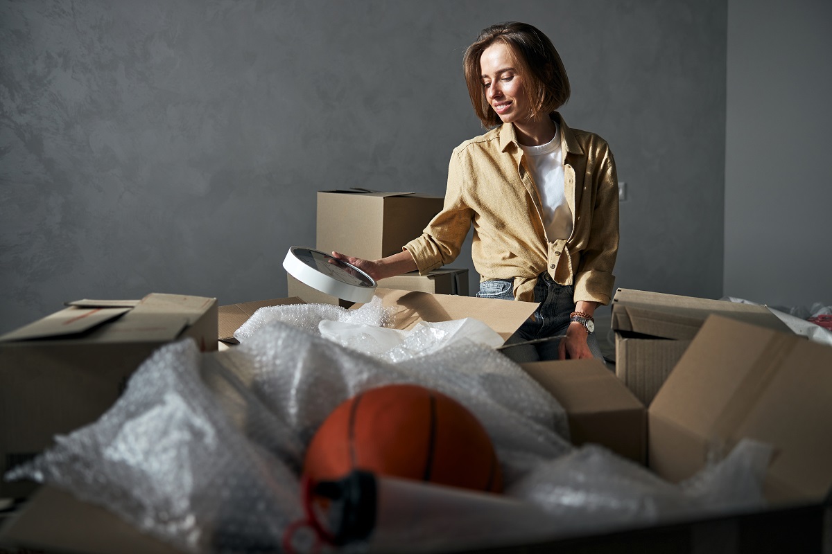 Cheerful female with a wall clock in one hand seated among the open cardboard boxes